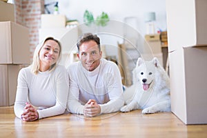 Young beautiful couple with dog lying down on the floor at new home around cardboard boxes