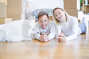 Young beautiful couple with dog lying down on the floor at new home around cardboard boxes