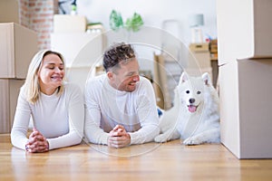 Young beautiful couple with dog lying down on the floor at new home around cardboard boxes