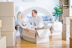 Young beautiful couple with dog sitting on the floor at new home around cardboard boxes
