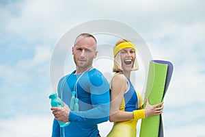 Young beautiful couple doing sports exercises. Strong handsome man holding bottle of water standing next to young