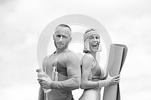 Young beautiful couple doing sports exercises. Strong handsome man holding bottle of water standing next to young