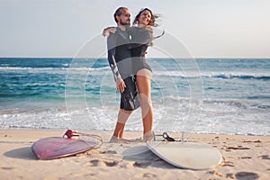 Young beautiful couple of friends are hugging by the ocean with surfboards on the sand, sport