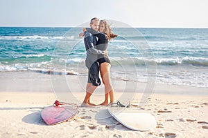 Young beautiful couple of friends are hugging by the ocean with surfboards on the sand, sport