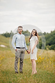 Young beautiful couple hand by hand walking in the field in summer. woman with long hair and man with stylish haircut