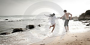 Young beautiful couple having fun jumping along beach