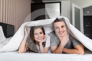 Young beautiful couple having fun lying on the bed under the blanket in the morning. Relationship concept