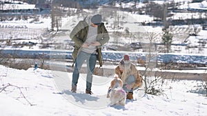 Young beautiful couple having fun with small active dog on a snowy hill