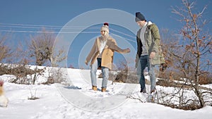 Young beautiful couple having fun with small active dog on a snowy hill