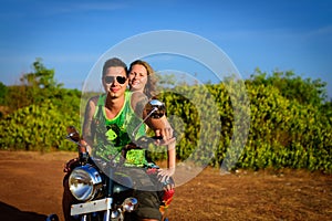 Young beautiful couple hipsters in stylish clothing on the motorcycle posing against a blue sky and green grass. Adventure trip