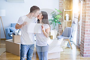 Young beautiful couple holding banner at new home around cardboard boxes