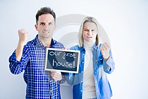 Young beautiful couple holding blackboard standing over isolated white background annoyed and frustrated shouting with anger,