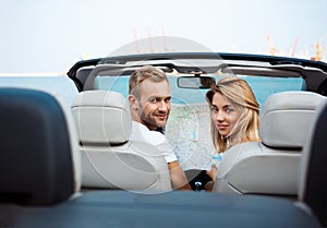 Young beautiful couple holding map, sitting in car near seacoast