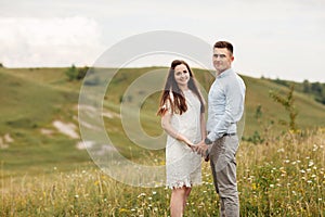 Young beautiful couple is hugging in the field in summer. woman with long hair and man with stylish haircut