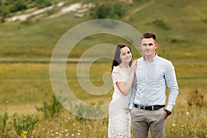 Young beautiful couple is hugging in the field in summer. woman with long hair and man with stylish haircut