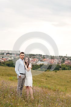 Young beautiful couple is hugging in the field in summer. woman with long hair and man with stylish haircut