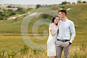 Young beautiful couple is hugging in the field in summer. woman with long hair and man with stylish haircut