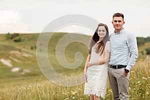 Young beautiful couple is hugging in the field in summer. woman with long hair and man with stylish haircut