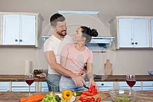 Young beautiful couple hugging in the kitchen cooking together a salad. They smile at each other