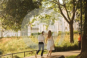 Young beautiful couple, husband in a white shirt and a wife in a dress walking around the park in summer time
