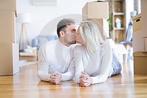 Young beautiful couple kissing lying down on the floor at new home around cardboard boxes