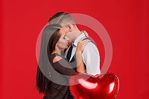 A young and beautiful couple kissing on a red background. The concept of Valentine`s Day.