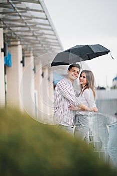 Young beautiful couple looking at each other with love under the umbrella in rainy day in the street. Love and couple relationship