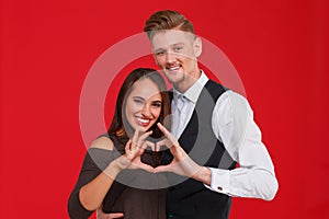 Young and beautiful couple in love make a heart on a red background. The concept of Valentine`s Day