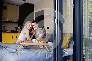 Young beautiful couple in love is sitting in bed and having healthy breakfast together.