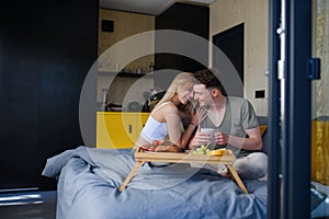 Young beautiful couple in love is sitting in bed and having healthy breakfast together.