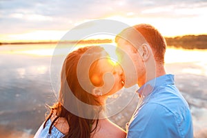 Young beautiful couple in love staying and kissing on the beach on sunset. Soft sunny colors.