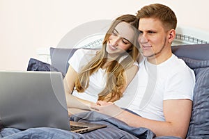 Young beautiful couple lying on bed in bedroom and using laptop