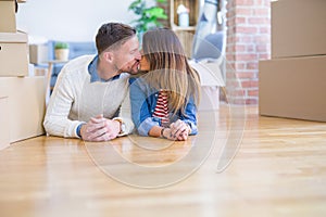 Young beautiful couple lying down on the floor kissing at new home around cardboard boxes