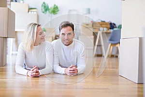 Young beautiful couple lying down on the floor at new home around cardboard boxes