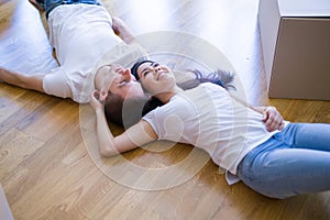 Young beautiful couple lying down at new home around cardboard boxes