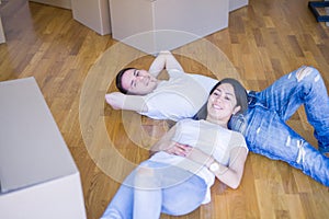 Young beautiful couple lying down at new home around cardboard boxes