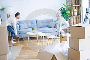 Young beautiful couple moving sofa at new home around cardboard boxes