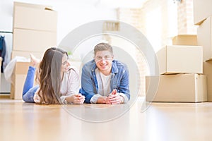 Young beautiful couple relaxing lying on the floor around cardboard boxes at home, smiling happy moving to a new house