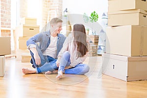 Young beautiful couple relaxing sitting on the floor around cardboard boxes at home, smiling happy moving to a new house