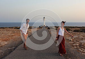 Young beautiful couple`s portrait with Cap de Barberia`s lighthouse on soft background, Formentera, Balearic Islands, Spain