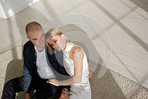 a young beautiful couple is sitting on the floor on the carpet, gently touching each other, enjoying the moment