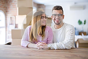 Young beautiful couple sitting on the table at home, hugging in love very happy for moving to new home with cardboard boxes behind