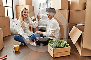 Young beautiful couple smiling happy celebrating with hands raised up at new home