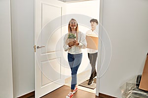 Young beautiful couple smiling happy holding cardboard box entering at new home