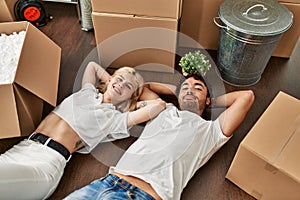 Young beautiful couple smiling happy relaxing with hands on head lying on the floor at new home