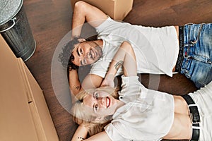 Young beautiful couple smiling happy relaxing with hands on head lying on the floor at new home