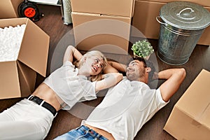 Young beautiful couple smiling happy relaxing with hands on head lying on the floor at new home