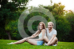 Young beautiful couple smiling, sitting on grass in park. Outdoor background.