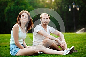 Young beautiful couple smiling, sitting on grass in park. Outdoor background.