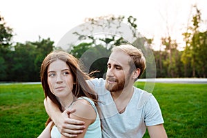 Young beautiful couple smiling, sitting on grass in park. Outdoor background.